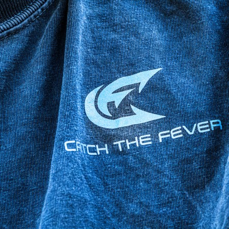 Close-up detail of the chest logo on a dark gray Catch The Fever® Crappie short sleeve lifestyle T shirt, showing the Catch The Fever® emblem and text.