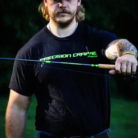 Catch The Fever Marketing Director Dillon Weaver holding a Precision Crappie™ fishing rod while wearing a black Precision Crappie t-shirt with green logo and a Catch The Fever hat.