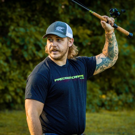 Catch The Fever Marketing Director Dillon Weaver holding a Precision Crappie™ fishing rod while wearing a black Precision Crappie t-shirt with green logo and a Catch The Fever hat.