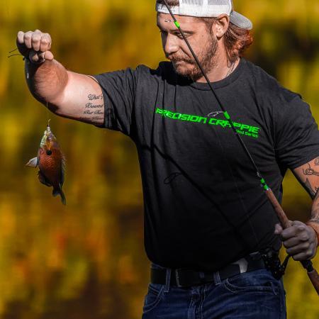 Catch The Fever Marketing Director Dillon Weaver holding a Precision Crappie™ fishing rod while wearing a black Precision Crappie t-shirt with green logo and a Catch The Fever hat.