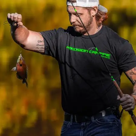 Catch The Fever Marketing Director Dillon Weaver holding a Precision Crappie™ fishing rod while wearing a black Precision Crappie t-shirt with green logo and a Catch The Fever hat.